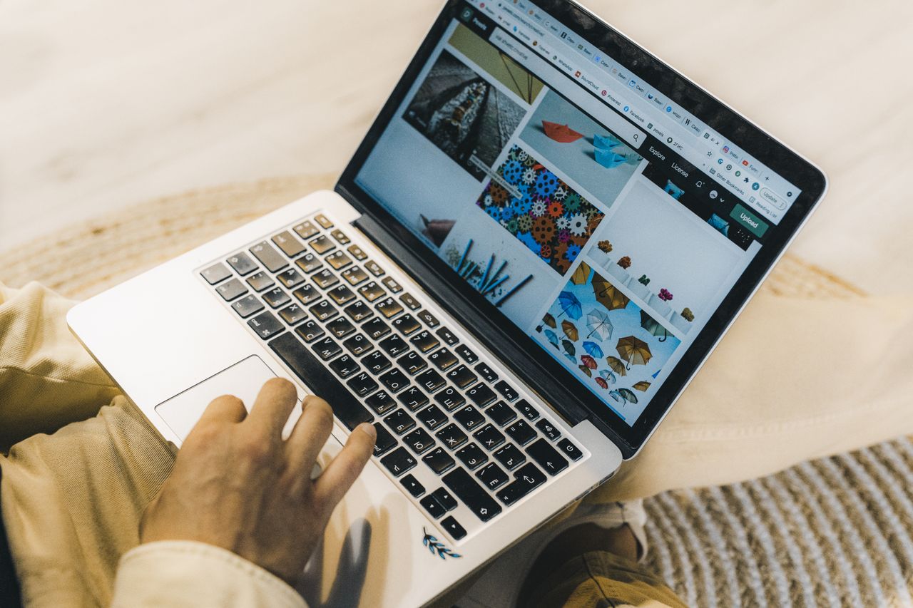Une personne utilise un ordinateur portable pour parcourir des sites de photos de stock. Travail en freelance dans un cadre chaleureux.